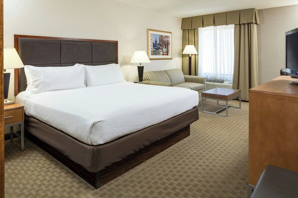 A hotel room with a large bed, a desk, a chair, a television, and a window with curtains.