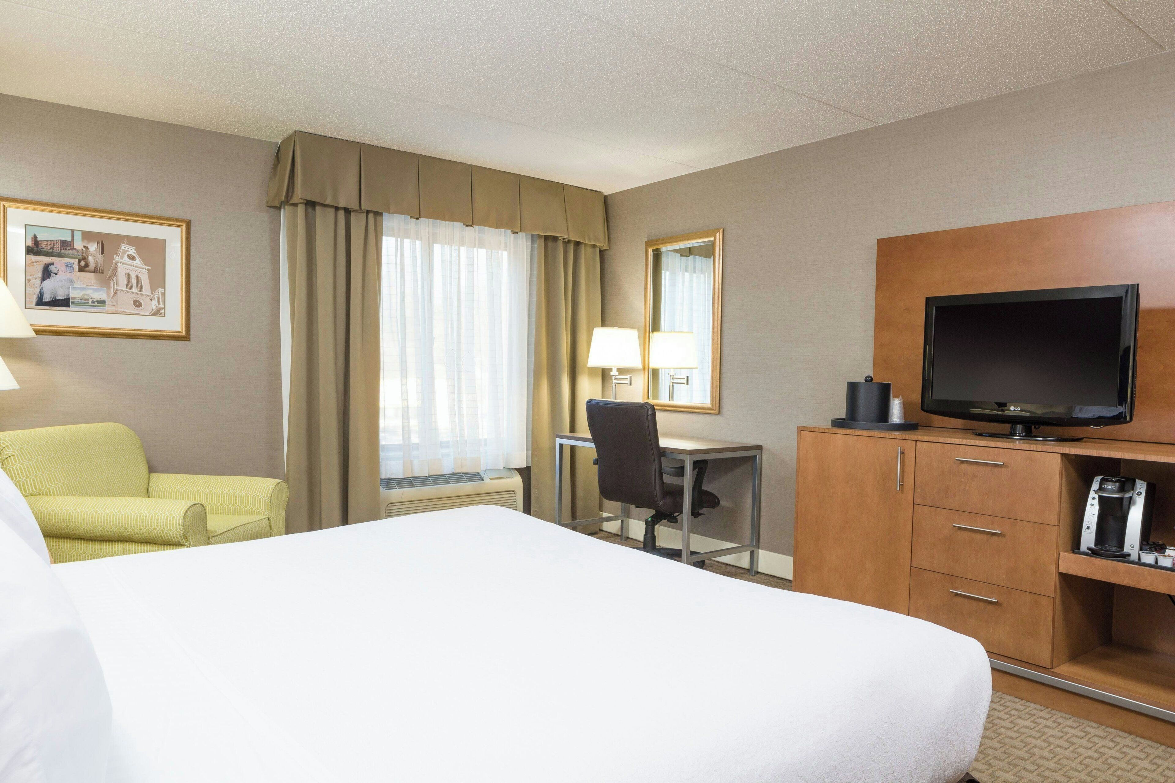 A hotel room with a bed, a desk, a chair, a television, and a framed picture on the wall.