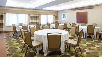 A conference room with multiple tables and chairs, large windows with curtains, and a patterned carpet.