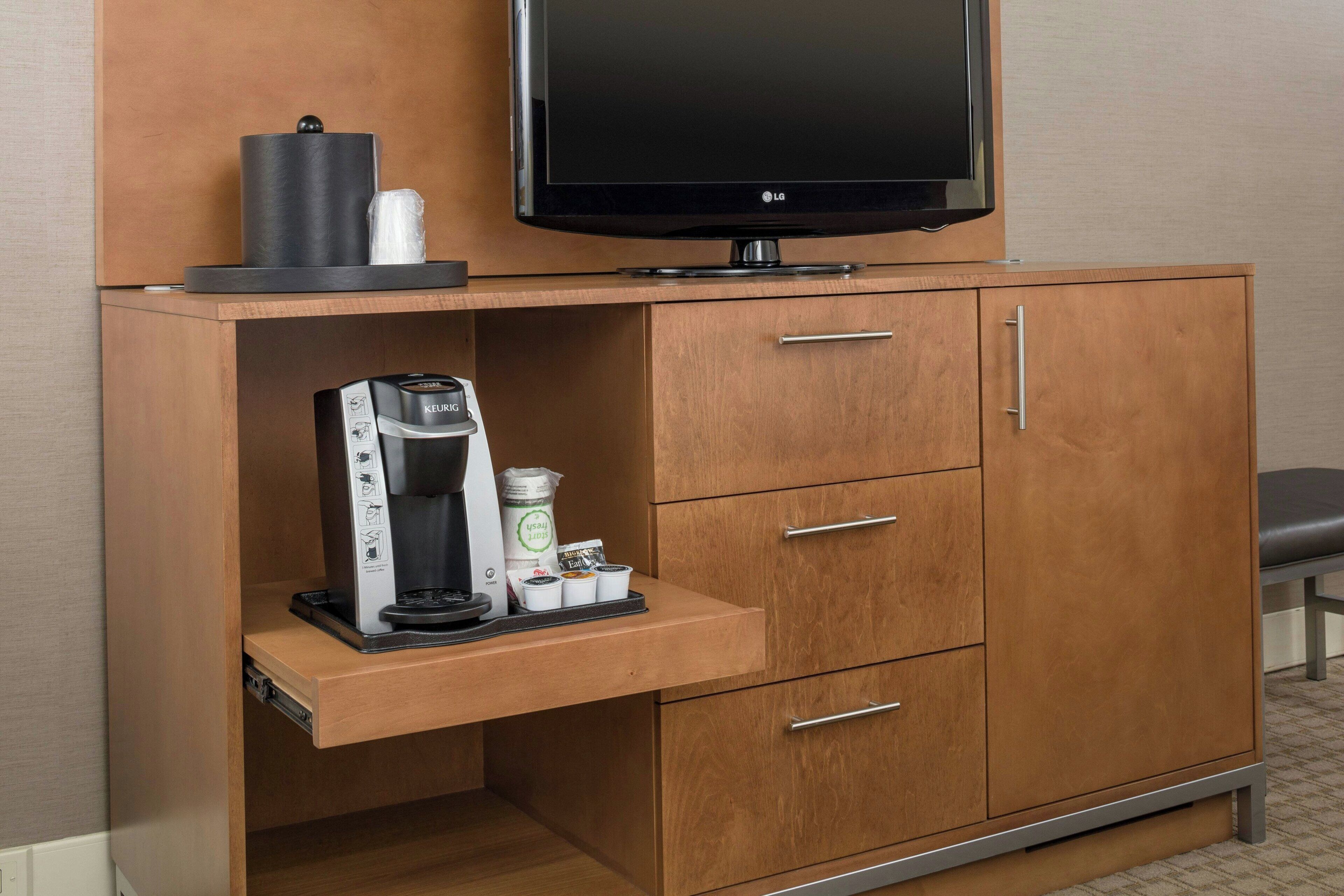 A wooden cabinet with a flat-screen TV, a coffee maker, and a small refrigerator.