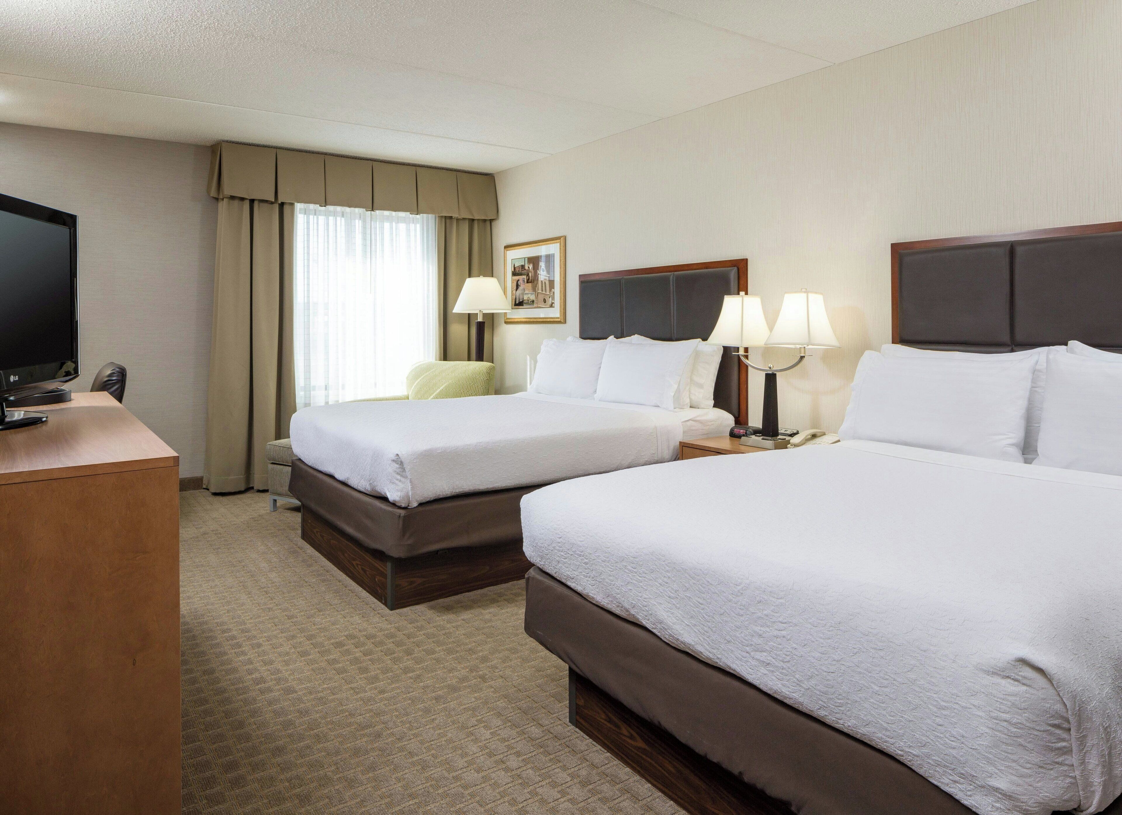 A hotel room with two beds, a desk with a TV, a lamp, and a framed picture on the wall.