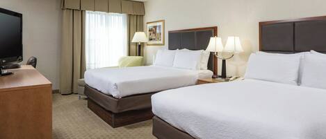 A hotel room with two beds, a desk with a TV, a lamp, and a framed picture on the wall.