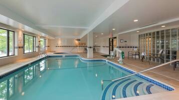 An indoor swimming pool with clear water, a tiled deck, and a seating area with chairs and tables.