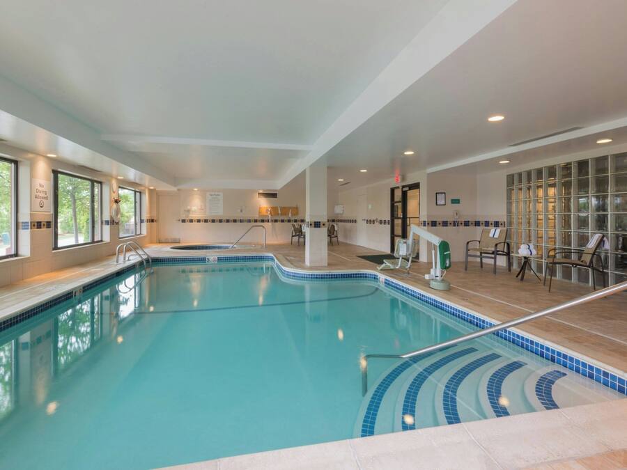 An indoor swimming pool with clear water, a tiled deck, and a seating area with chairs and tables.
