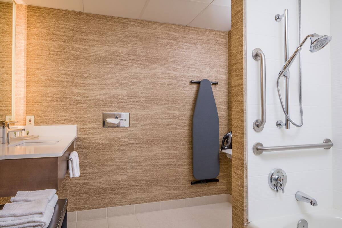 A modern bathroom with a textured wall, a towel rack, a shower with a handheld showerhead, and a toilet paper holder.