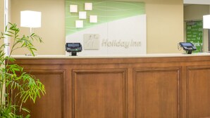 A reception desk with a Holiday Inn sign, a cash register, a phone, and a digital screen. - Holiday Inn Manchester Airport by IHG (Manchester)