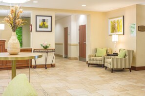 A hotel lobby with a reception desk, a vase with flowers, two striped armchairs, a table with a lamp, and a framed picture on the wall. - Holiday Inn Manchester Airport by IHG (Manchester)