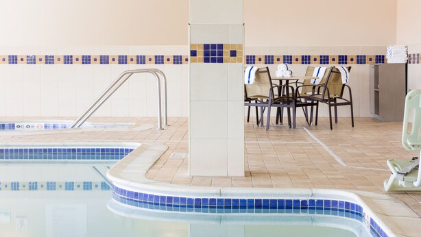 An indoor swimming pool with a tiled edge, a seating area with chairs and a table, and a small refrigerator. - Holiday Inn Manchester Airport by IHG (Manchester)
