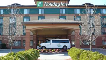 Ett Holiday Inn-hotell med en vit skåpbil parkerad framför, omgivet av välskötta buskar och träd.
