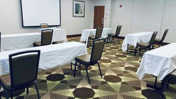 Un salón de conferencias con mesas, sillas, una pantalla de proyector y una alfombra estampada.