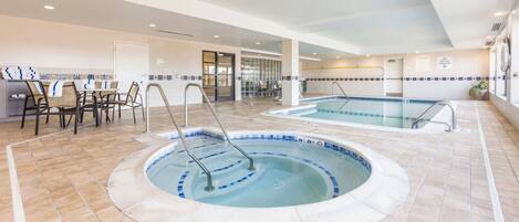 Un área de piscina interior con un jacuzzi, zona de estar y una piscina separada.
