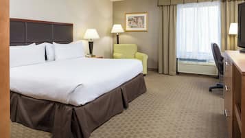 Une chambre d’hôtel avec un grand lit, un bureau, une chaise, une lampe et une fenêtre avec des rideaux.