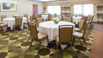 A conference room with multiple tables and chairs, arranged in a circular pattern, with a patterned carpet and a door in the background.