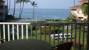 A balcony with a view of the ocean, palm trees, and a lawn with picnic tables. - Sea Village (Kailua-Kona)