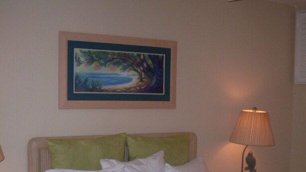 A hotel room with a bed, a nightstand, a lamp, and a painting on the wall. - Sea Village (Kailua-Kona)