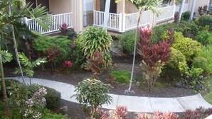 A landscaped courtyard with various plants and a pathway leading to a building with a balcony. - Sea Village (Kailua-Kona)