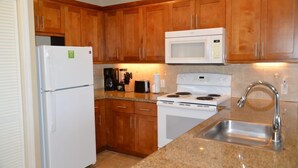 A kitchen with wooden cabinets, a white refrigerator, a microwave, a stove, and a sink. - Sea Village (Kailua-Kona)