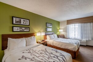 Habitación de hotel con dos camas, una mesita de noche con lámpara, una silla y una ventana con cortinas.
