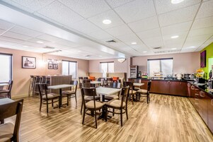 Un comedor moderno con varias mesas y sillas, una encimera de cocina con electrodomésticos y un ventanal que proporciona luz natural.