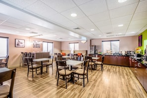 A modern dining area with multiple tables and chairs, a kitchen counter with appliances, and a large window providing natural light.