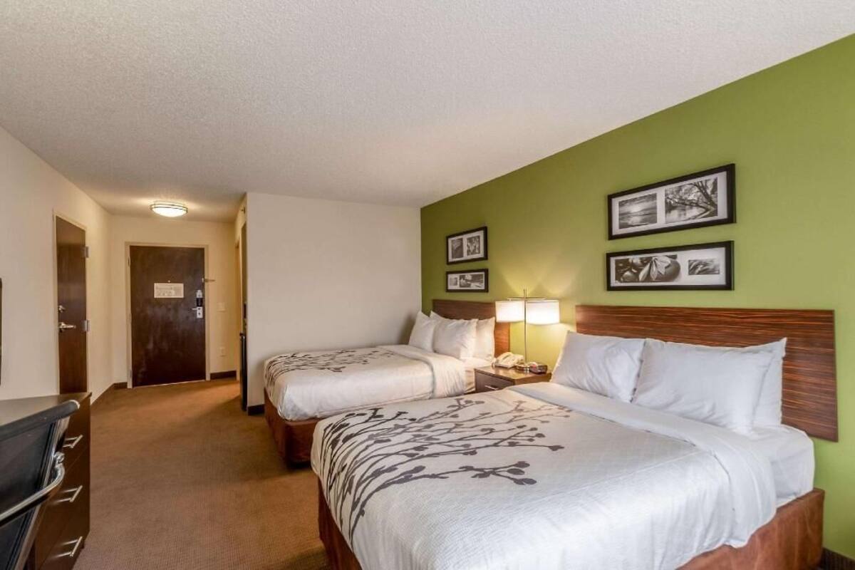 A hotel room with two beds, a desk, a chair, and a door.