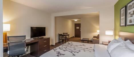 A hotel room with a bed, a desk with a chair, a television, and a dining area.