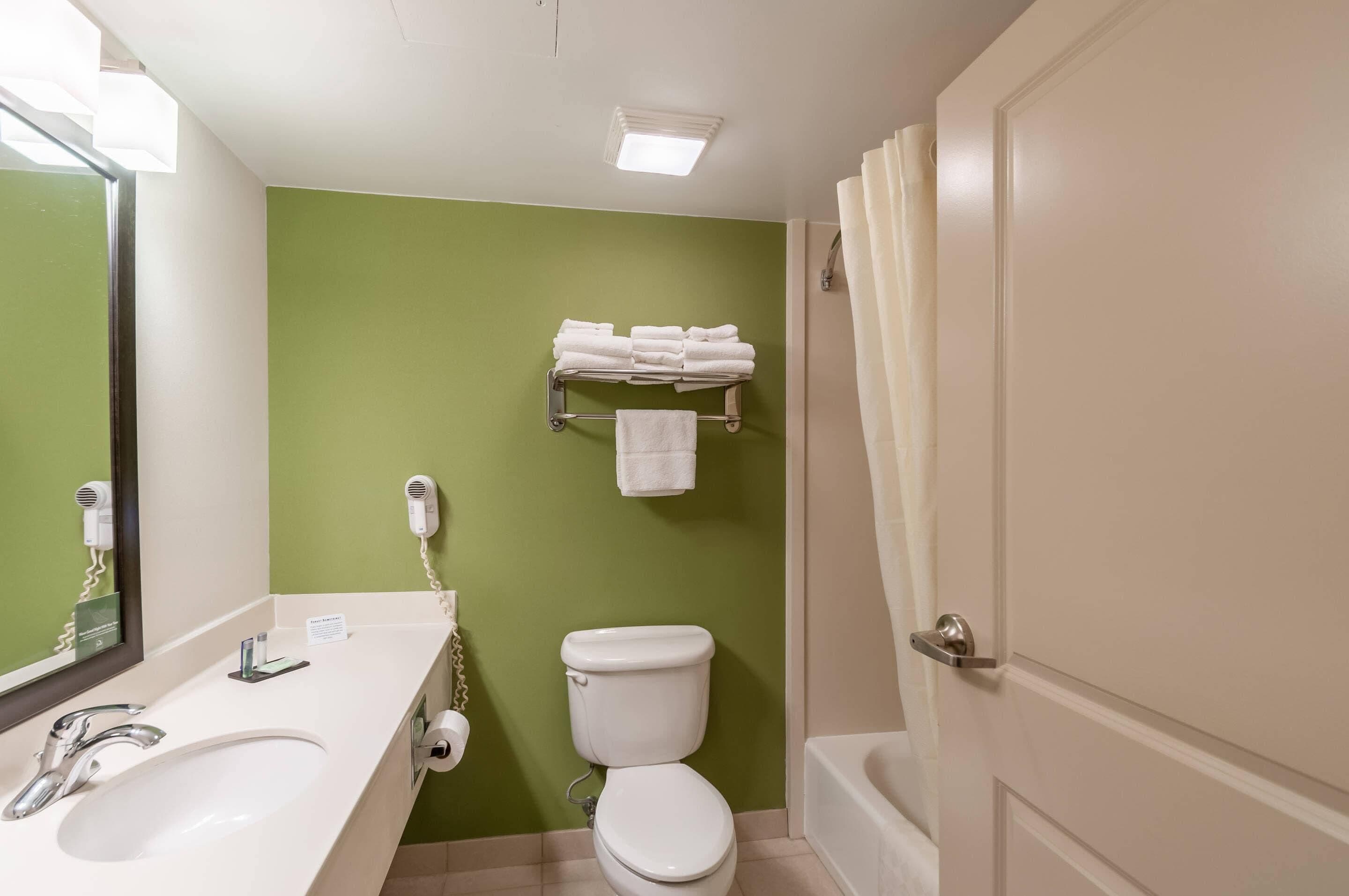 A bathroom with a white sink, a toilet, a shower, and a towel rack with folded towels.
