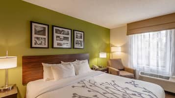 Habitación de hotel con cama, mesita de noche, silla, ventana con cortinas y tres cuadros en la pared.