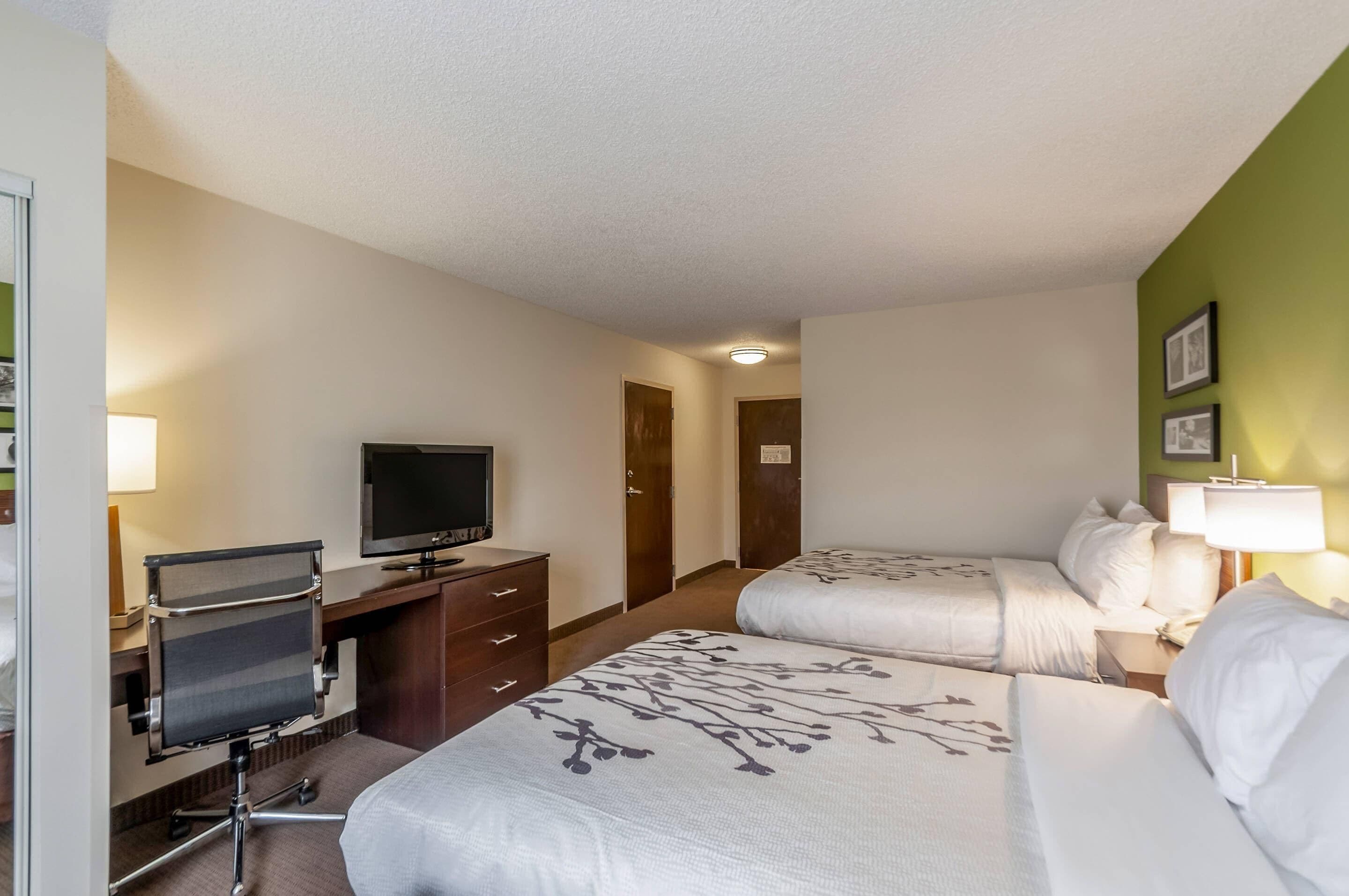 A hotel room with two beds, a desk with a computer, a television, and a door leading to another room.