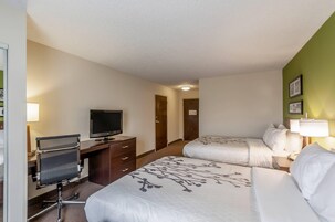 A hotel room with two beds, a desk with a computer, a television, and a door leading to another room.