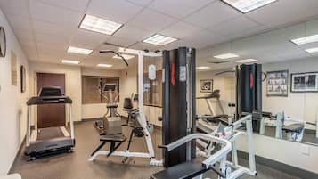 A gym with various exercise equipment, including treadmills, weight machines, and a bench.