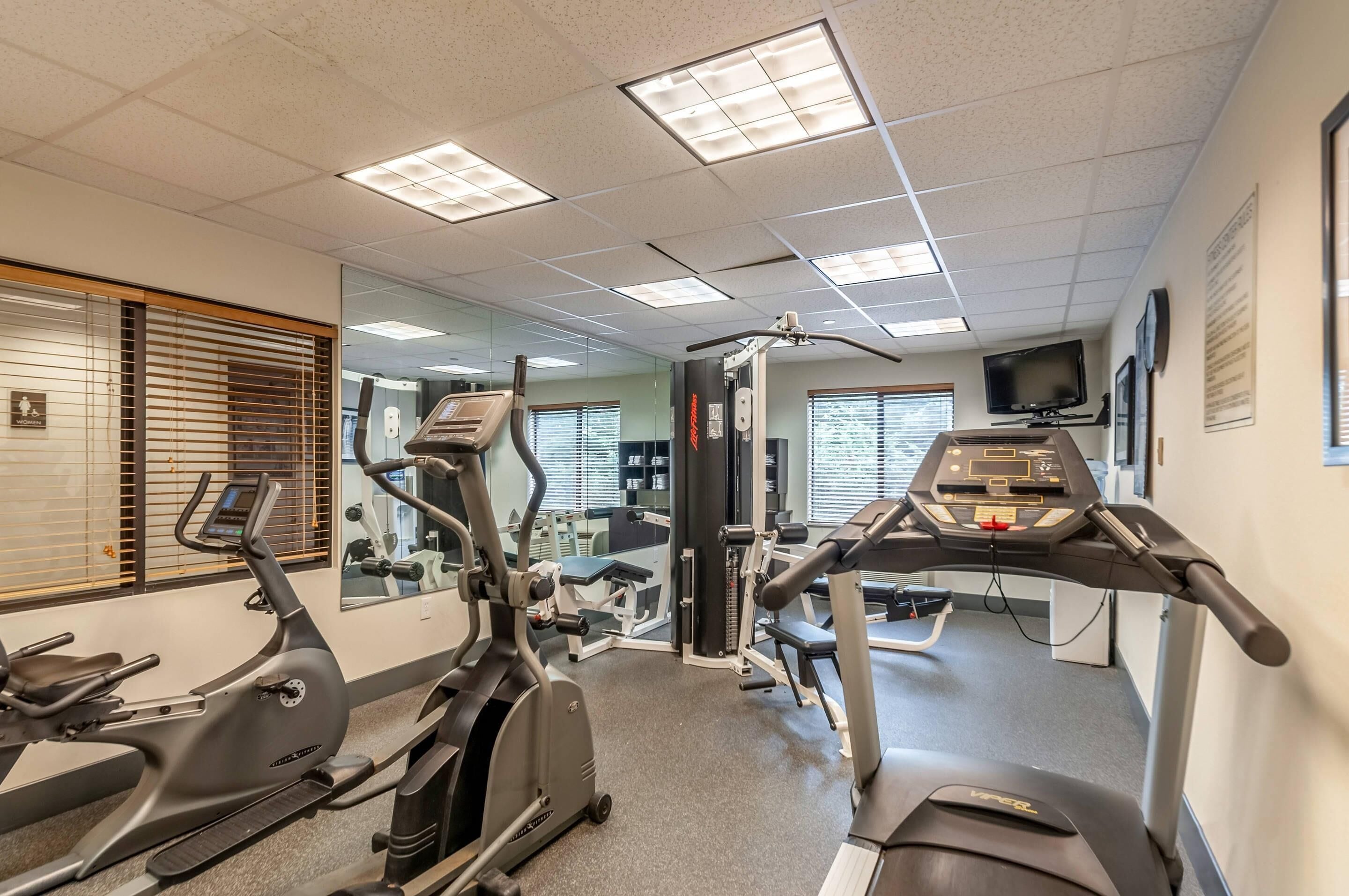 Un gimnasio con máquinas de cardio, espejos y una televisión.