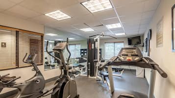 Un gimnasio con máquinas de cardio, espejos y una televisión.