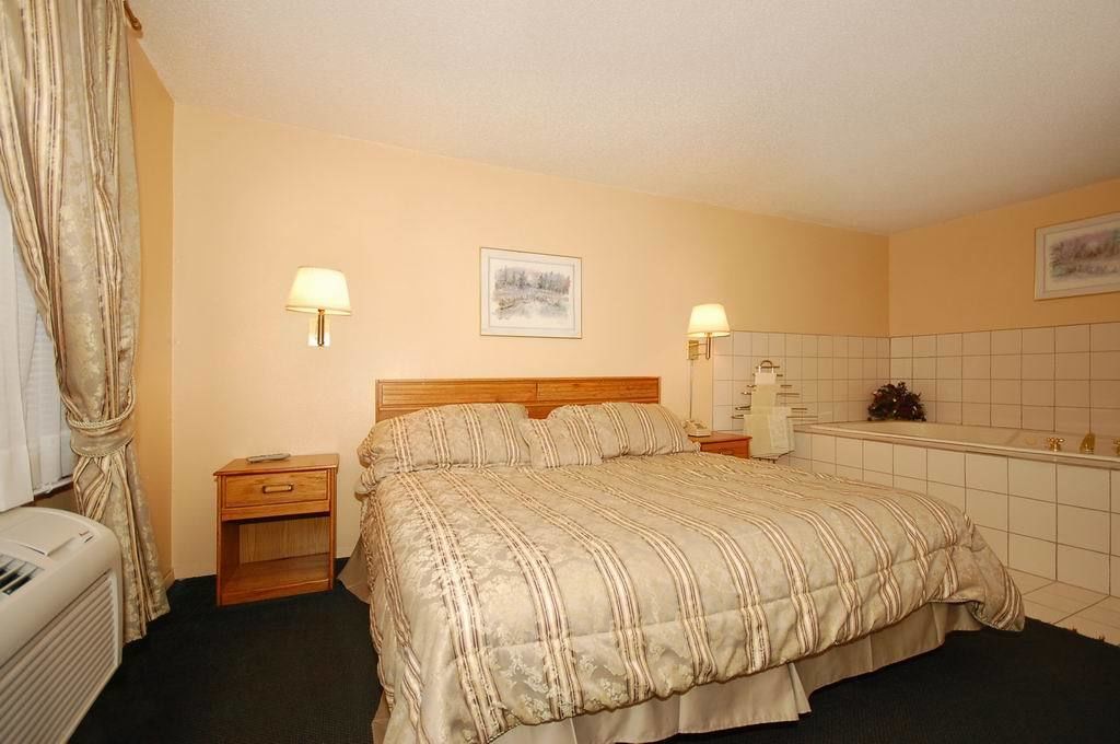 Ein Hotelzimmer mit Bett, Nachttischen, einer Lampe, einem Bild an der Wand und einem gefliesten Badezimmer.