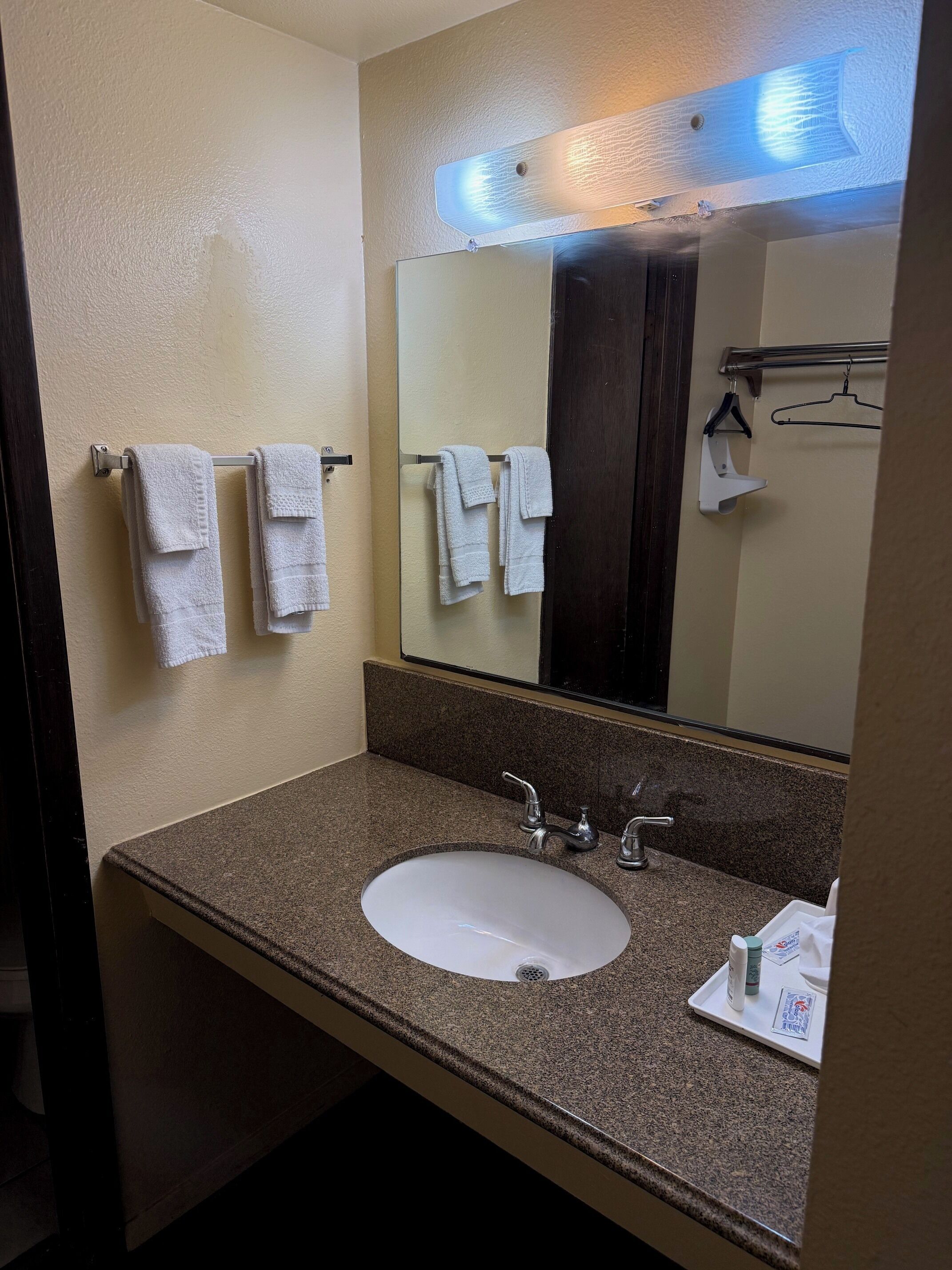 Une salle de bain avec un comptoir en granit, un lavabo blanc, deux porte-serviettes, un miroir et une serviette suspendue à l’un des porte-serviettes.