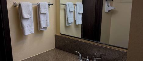 A bathroom with a granite countertop, a white sink, two towel racks, a mirror, and a towel hanging on one of the racks.
