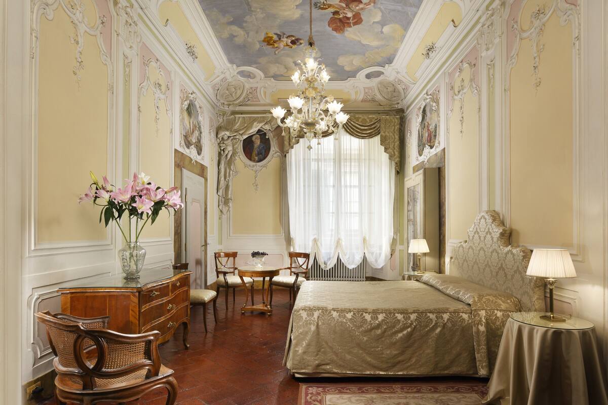 A luxurious bedroom with a large bed, ornate ceiling, and classic furniture.
