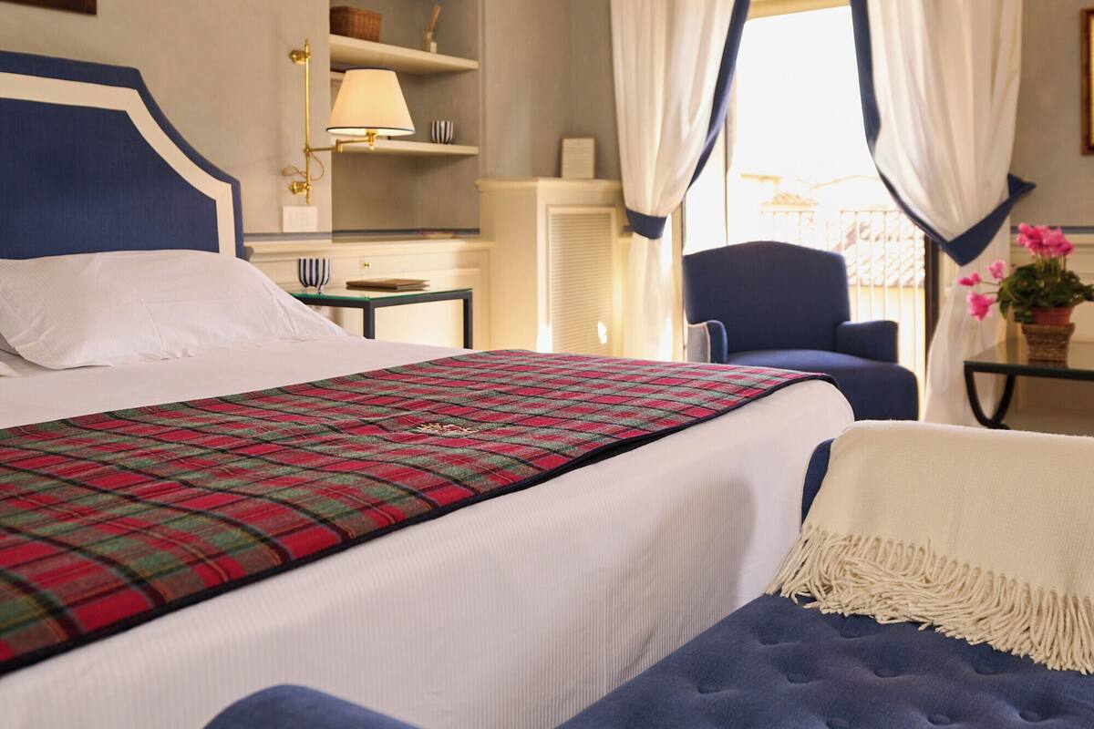A hotel room with a bed, a chair, a lamp, and a window with curtains.