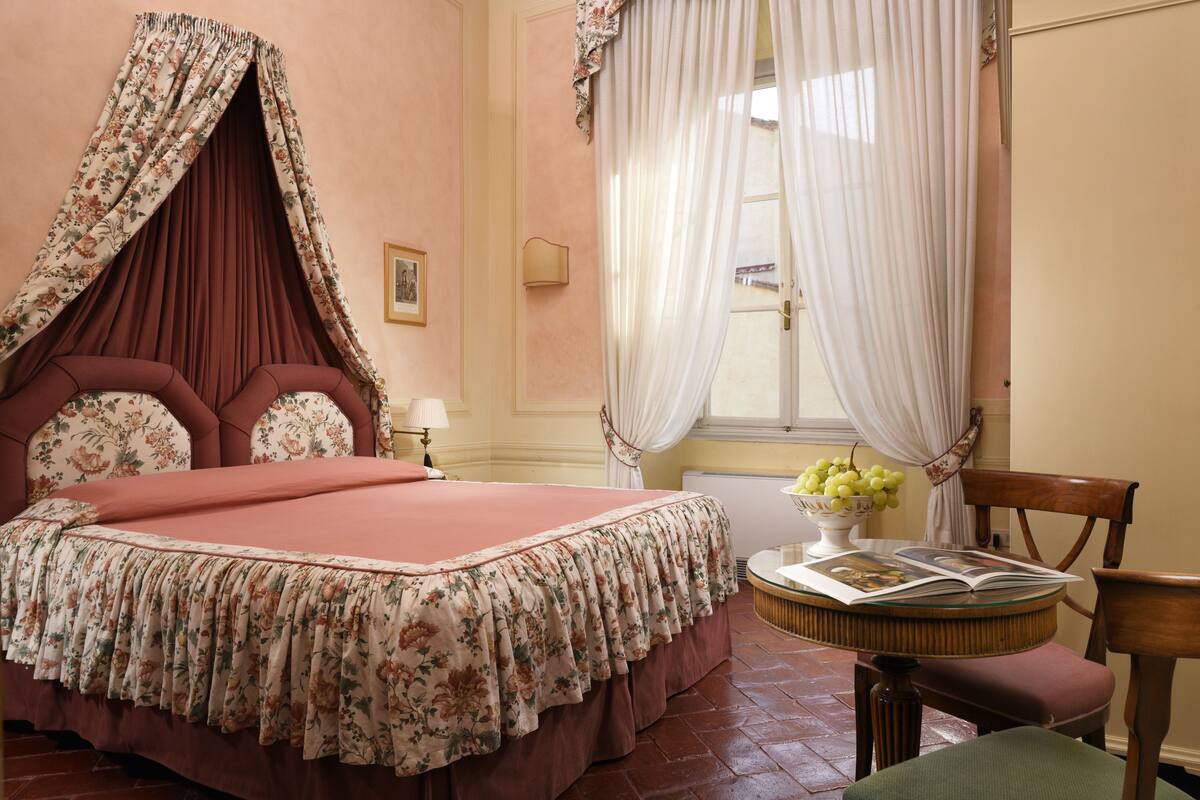 A bedroom with a four-poster bed, a round table with a vase of flowers, and a chair.