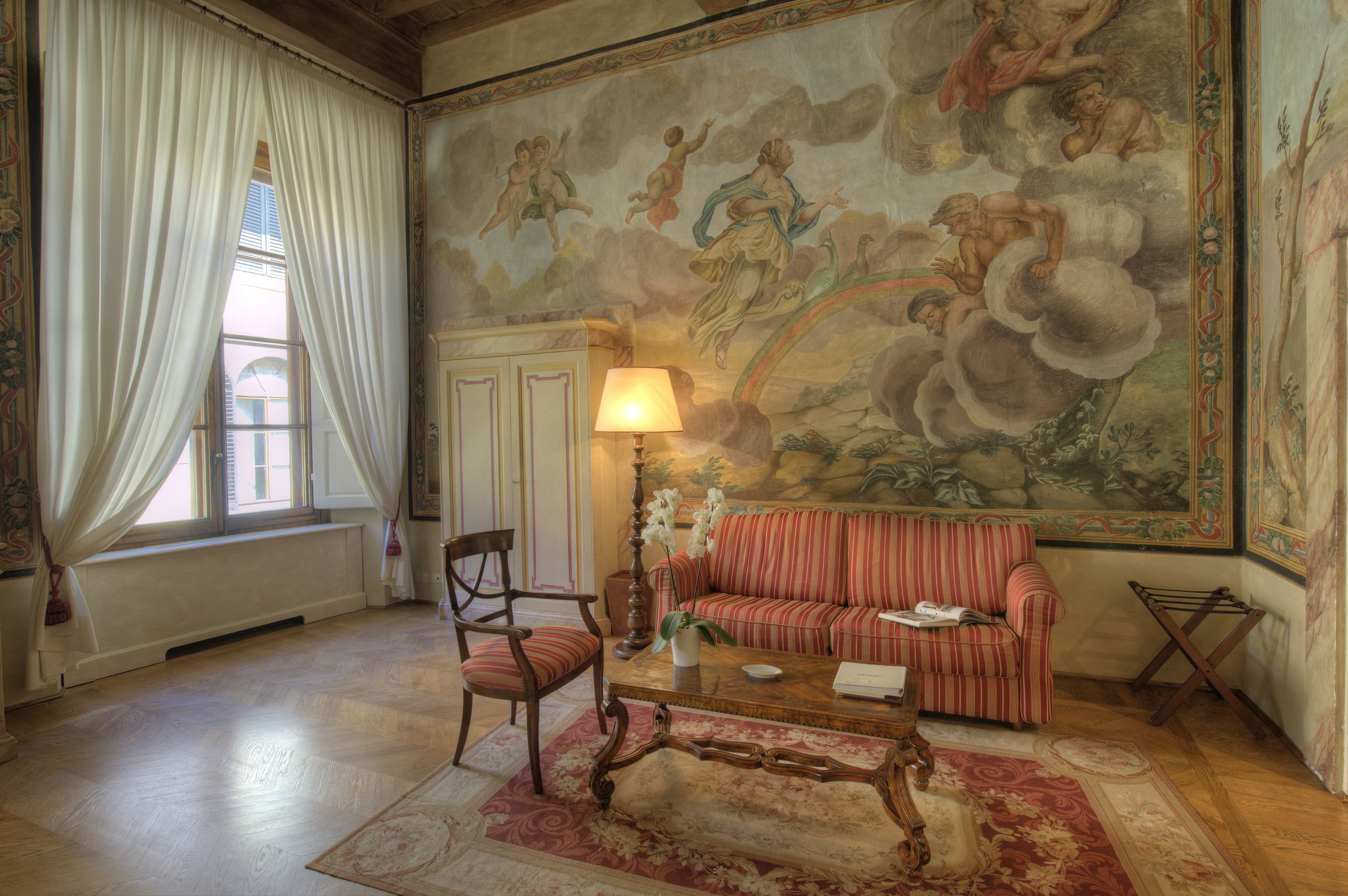 A room with a large mural, a sofa, a chair, a coffee table, and a lamp.
