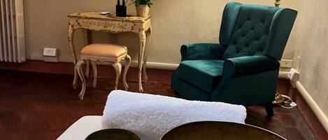 A room with a large mirror, a green armchair, a small table with a plant, and two large bowls on a white cloth.
