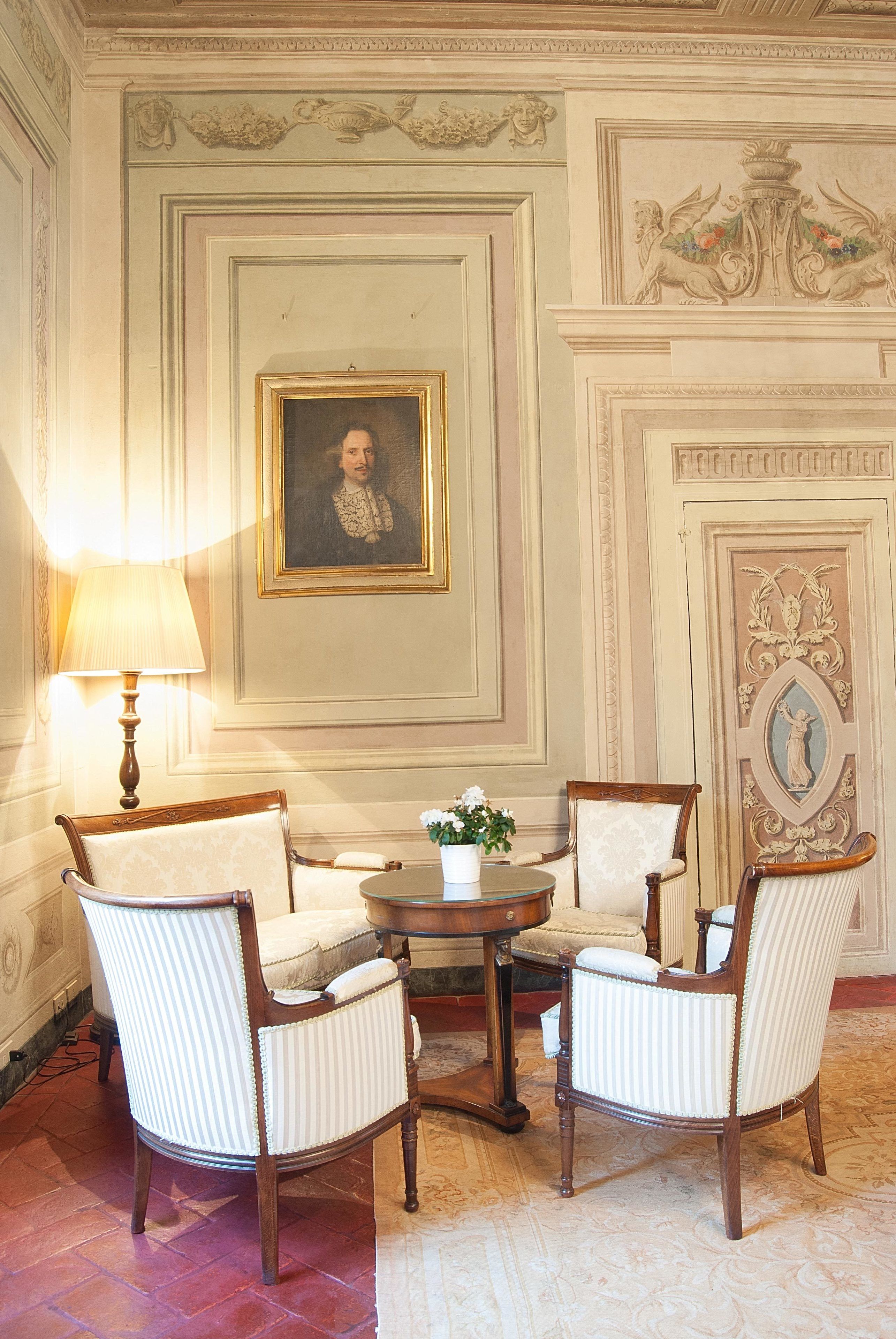 Une pièce comprenant une table ronde, deux fauteuils rembourrés, une lampe et un portrait encadré accroché au mur.