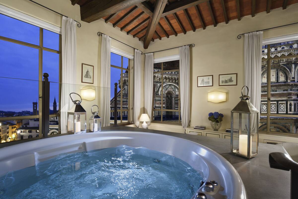 A hot tub in a room with large windows, decorative lighting, and framed pictures on the walls.
