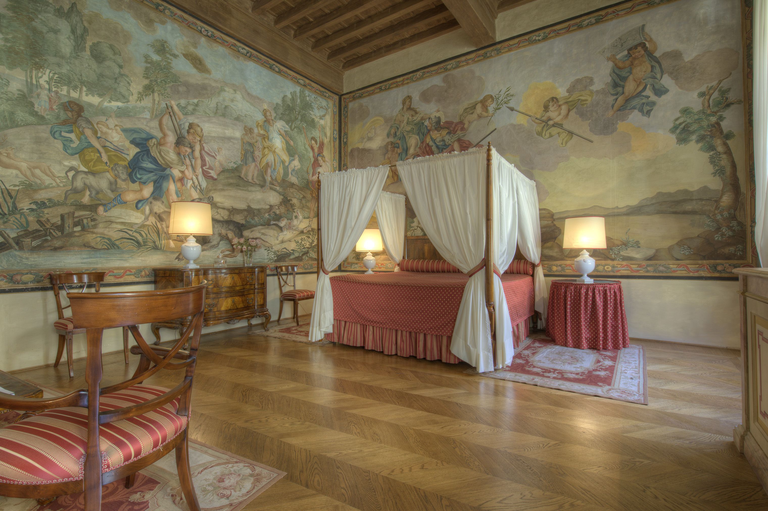 A bedroom with a four-poster bed, a mural on the walls, and a chandelier.