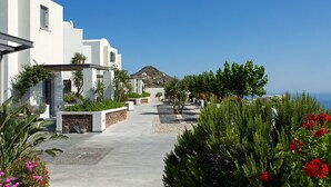 A coastal hotel with a paved walkway, white buildings, and lush greenery. - Xenones Filotera (Santorini)