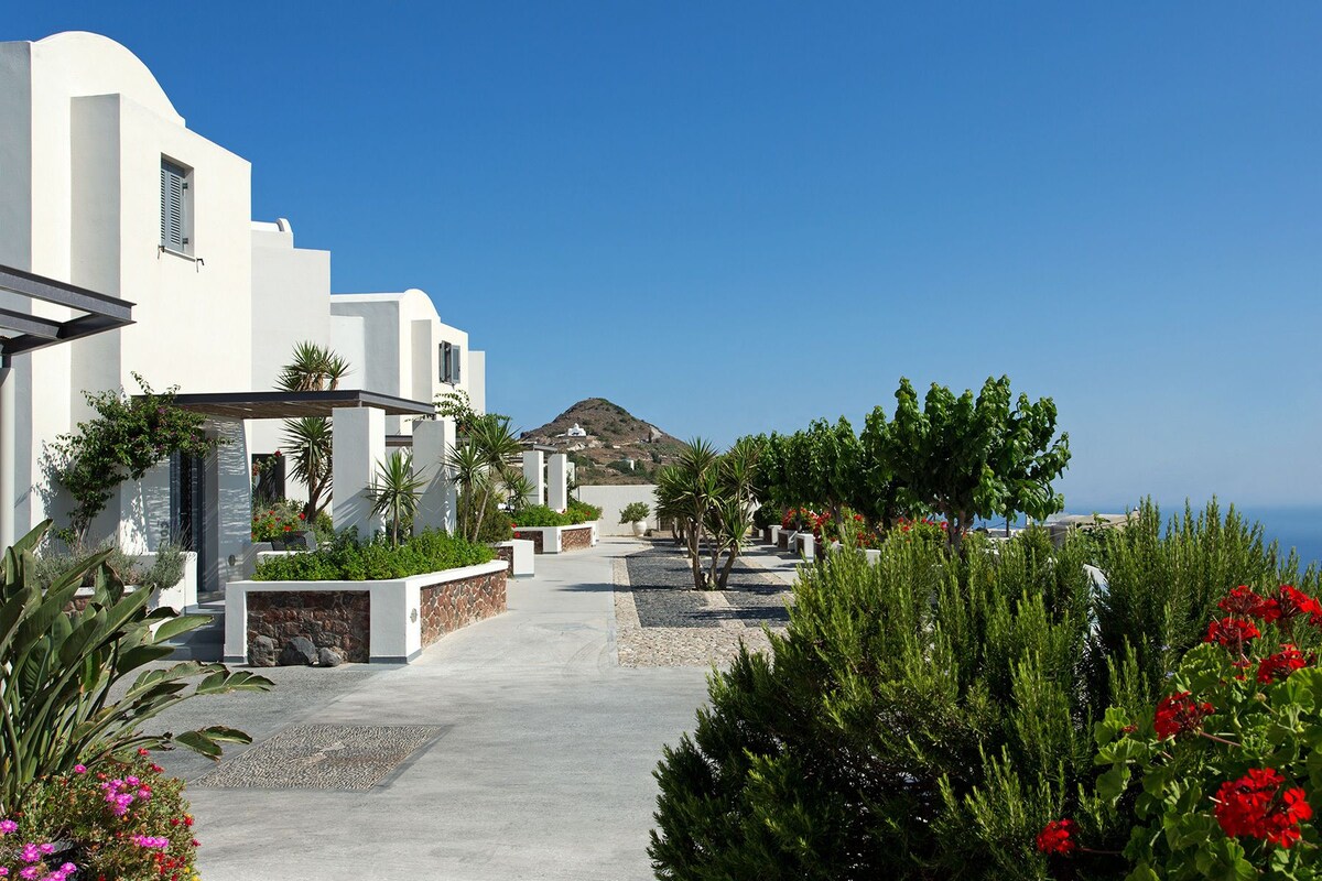 A coastal hotel with a paved walkway, white buildings, and lush greenery.