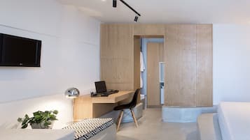 A modern bedroom with a bed, a desk, and a chair. There is a TV mounted on the wall and a plant on the floor.