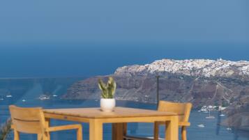 Mesa con sillas y una planta en maceta al frente, vista de un pueblo costero y el mar al fondo.