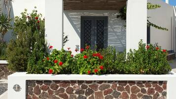 Un edificio moderno con fachada de piedra, una pérgola de madera y flores rojas en primer plano.