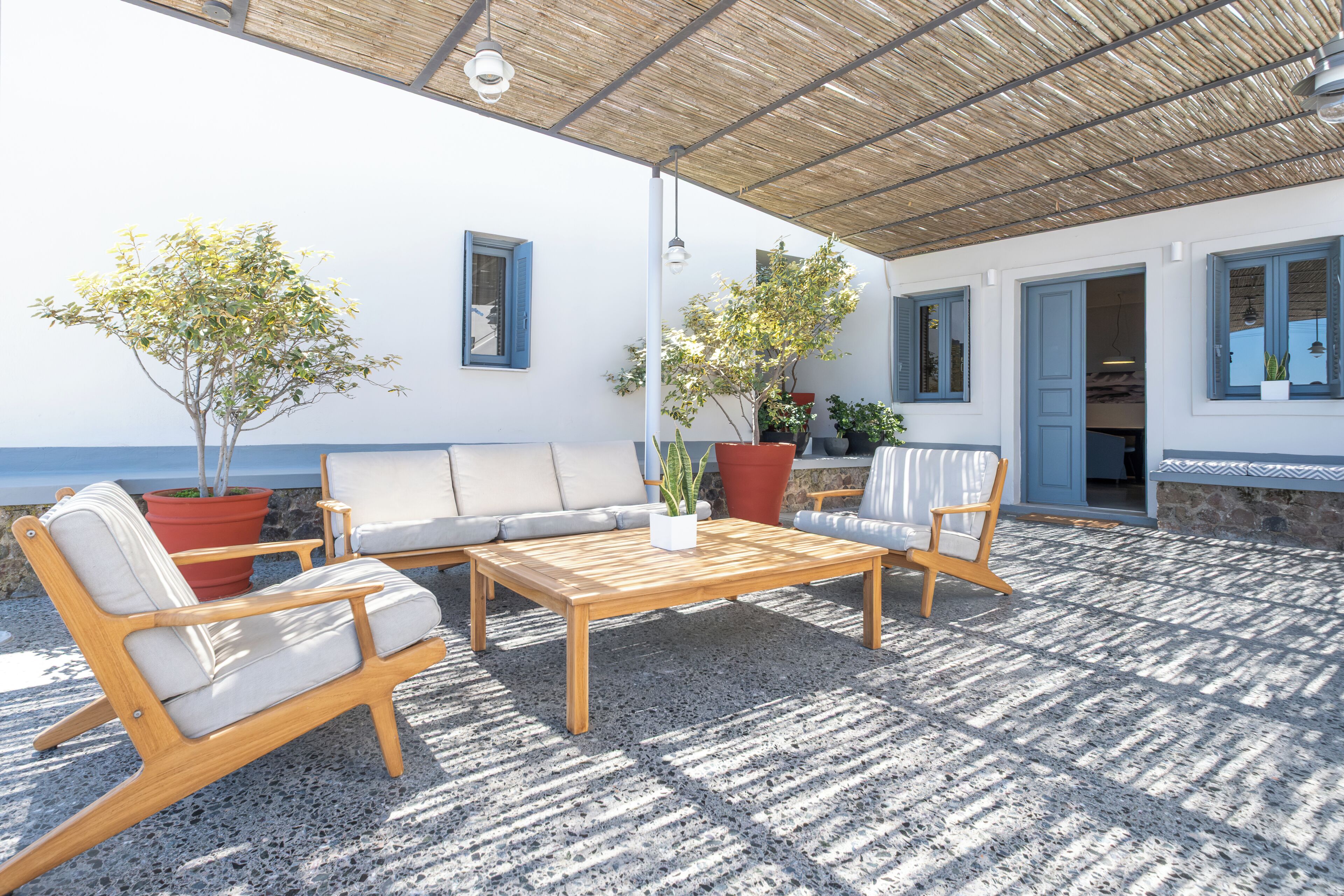 An outdoor seating area with a wooden table and chairs, potted plants, and a view of the sea.